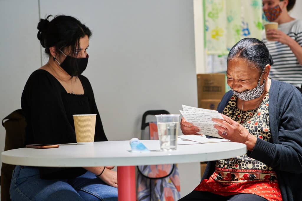 An elderly participant sits with a volunteer reading a hand-written letter