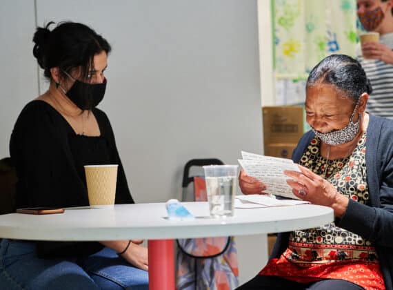 An elderly participant sits with a volunteer reading a hand-written letter